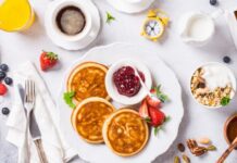 Healthy breakfast for two with coffee, pancakes, fresh berries, quick cereals and orange juice on light gray background, top view.