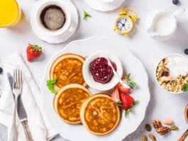 Healthy breakfast for two with coffee, pancakes, fresh berries, quick cereals and orange juice on light gray background, top view.